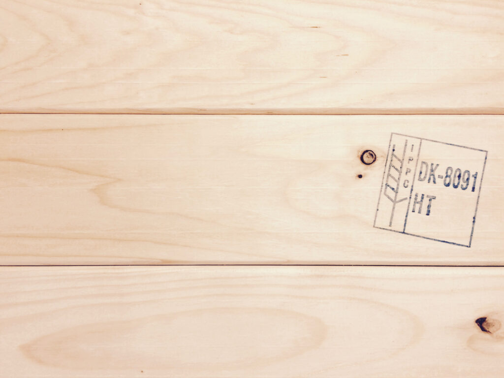 Light heat-treated wood with visible ISPM 15 HT mark (formerly IPPC) and natural knots in the surface.